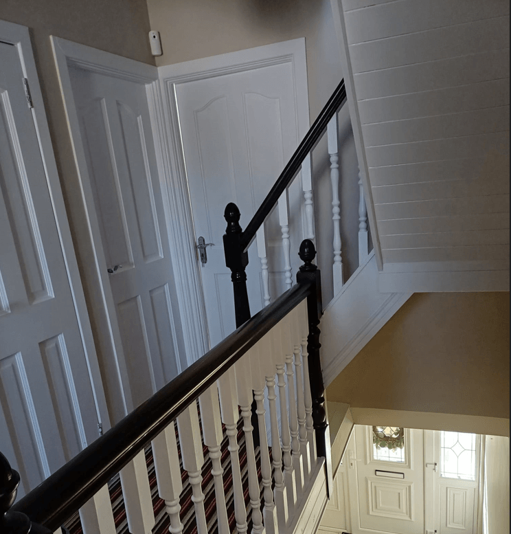 a staircase, painted white with black hand rail, hallway with doors, painted white.